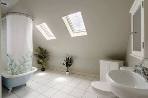 Un baño con bañera, inodoro y lavabo. Hay dos tragaluces en el techo.