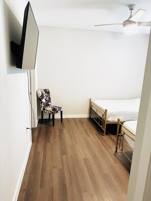 Un dormitorio con una cama, una silla, un ventilador de techo y un televisor montado en la pared.