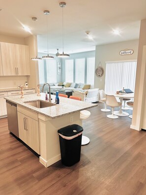 A modern kitchen with a central island, a dining area with a white table and chairs, and a living room with a sofa and a coffee table. - Spacious Family & Group Getaway near Airport (Austin)