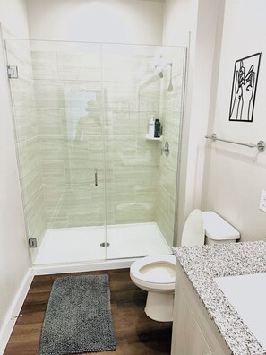 Et moderne badeværelse med en glasbrusekabine, toilet og bordplade i granit.