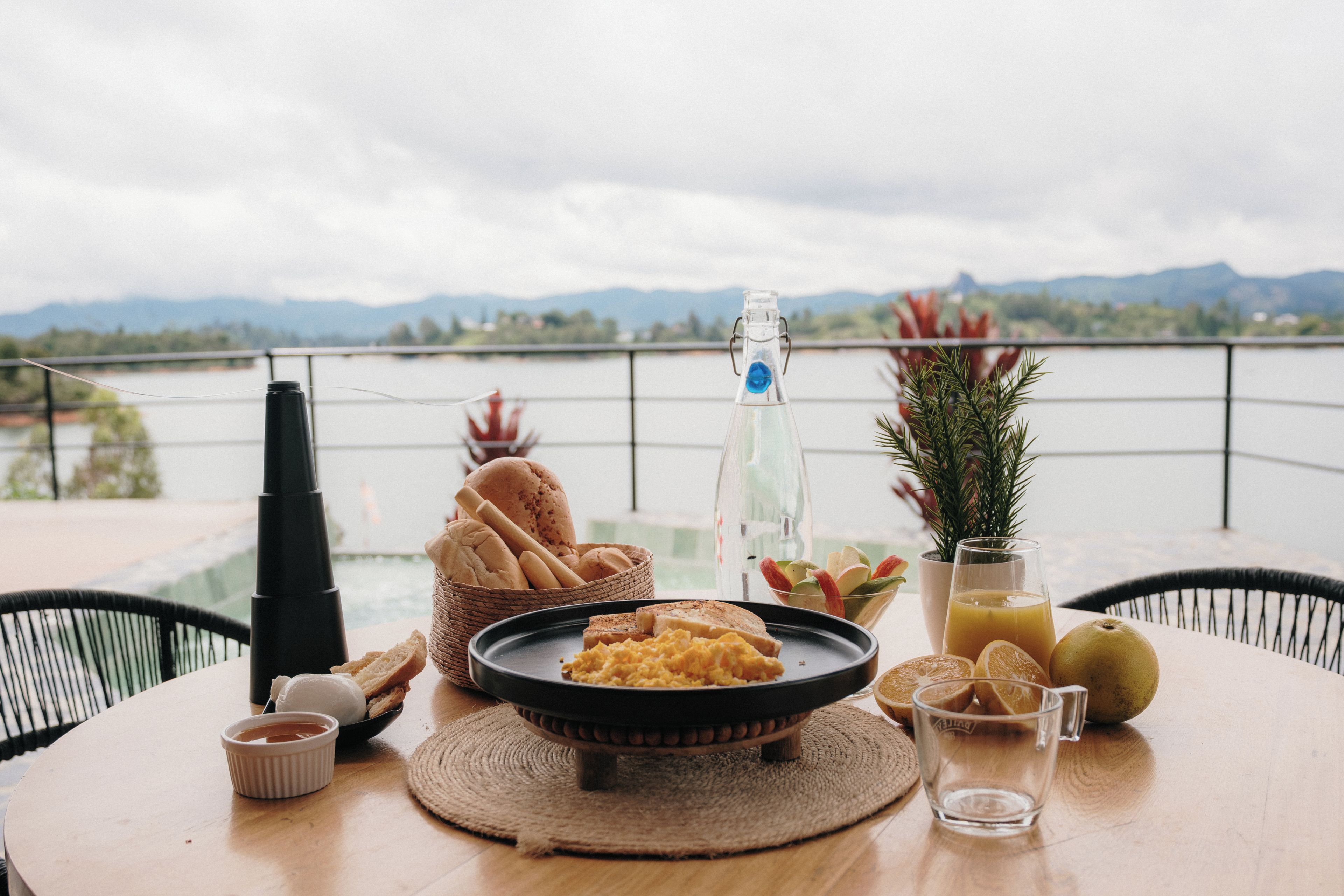 Una mesa con comida y bebidas, una botella, y vistas a un lago y montañas.
