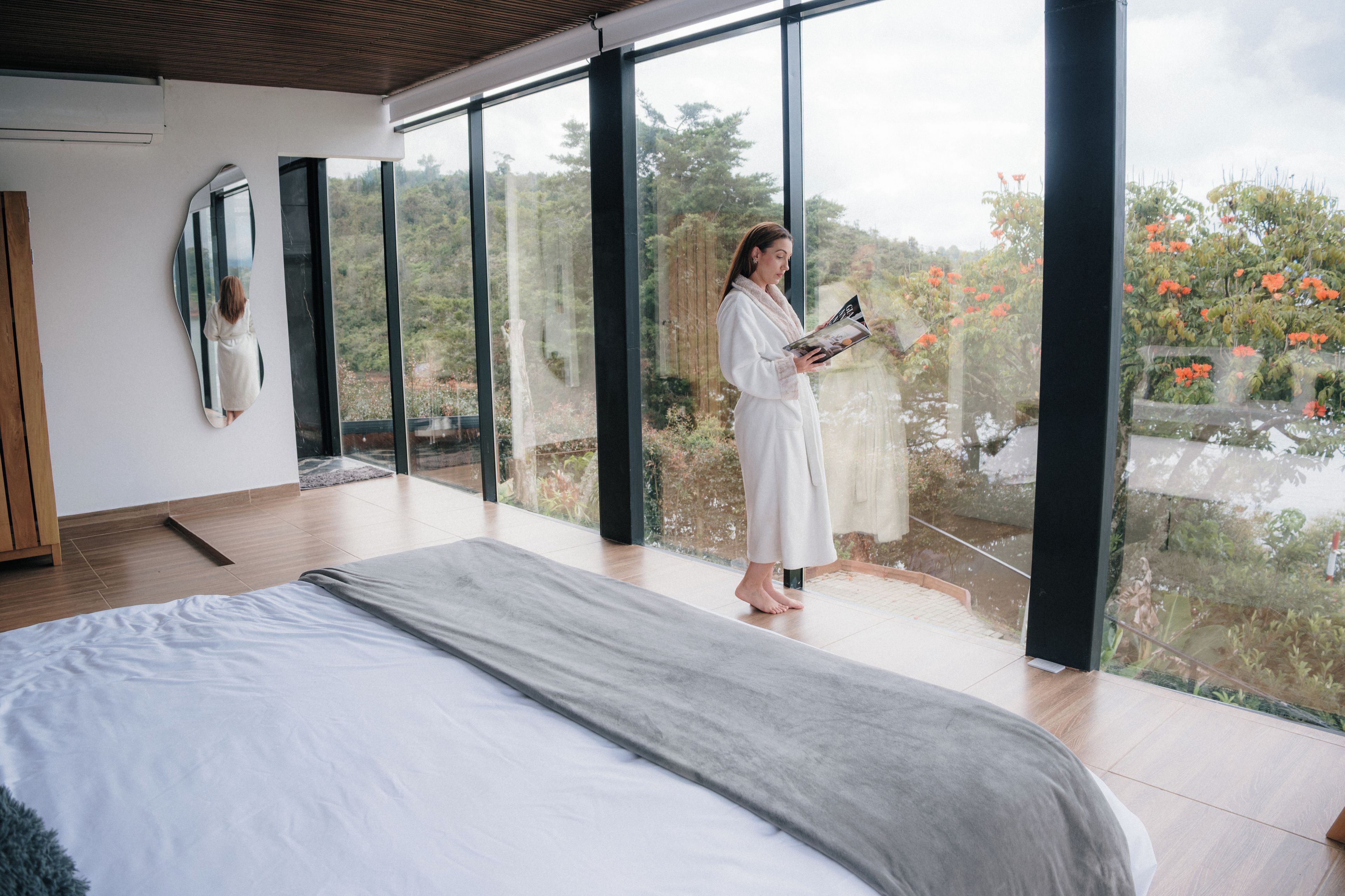 Un dormitorio moderno con una cama grande, un ventanal que da a un balcón y vistas a árboles y flores.