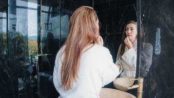 Une personne vêtue d’une robe blanche, debout devant un miroir de salle de bain, avec un mur en marbre en arrière-plan.
