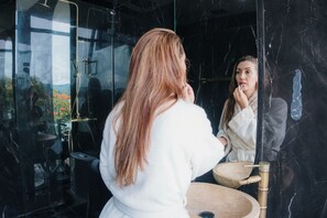 Una persona amb una bata blanca dreta davant d'un mirall de bany amb una paret de marbre.