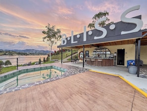 A modern building with a pool and outdoor seating area, overlooking a body of water and hills. - Bliss Club (El Peñol)