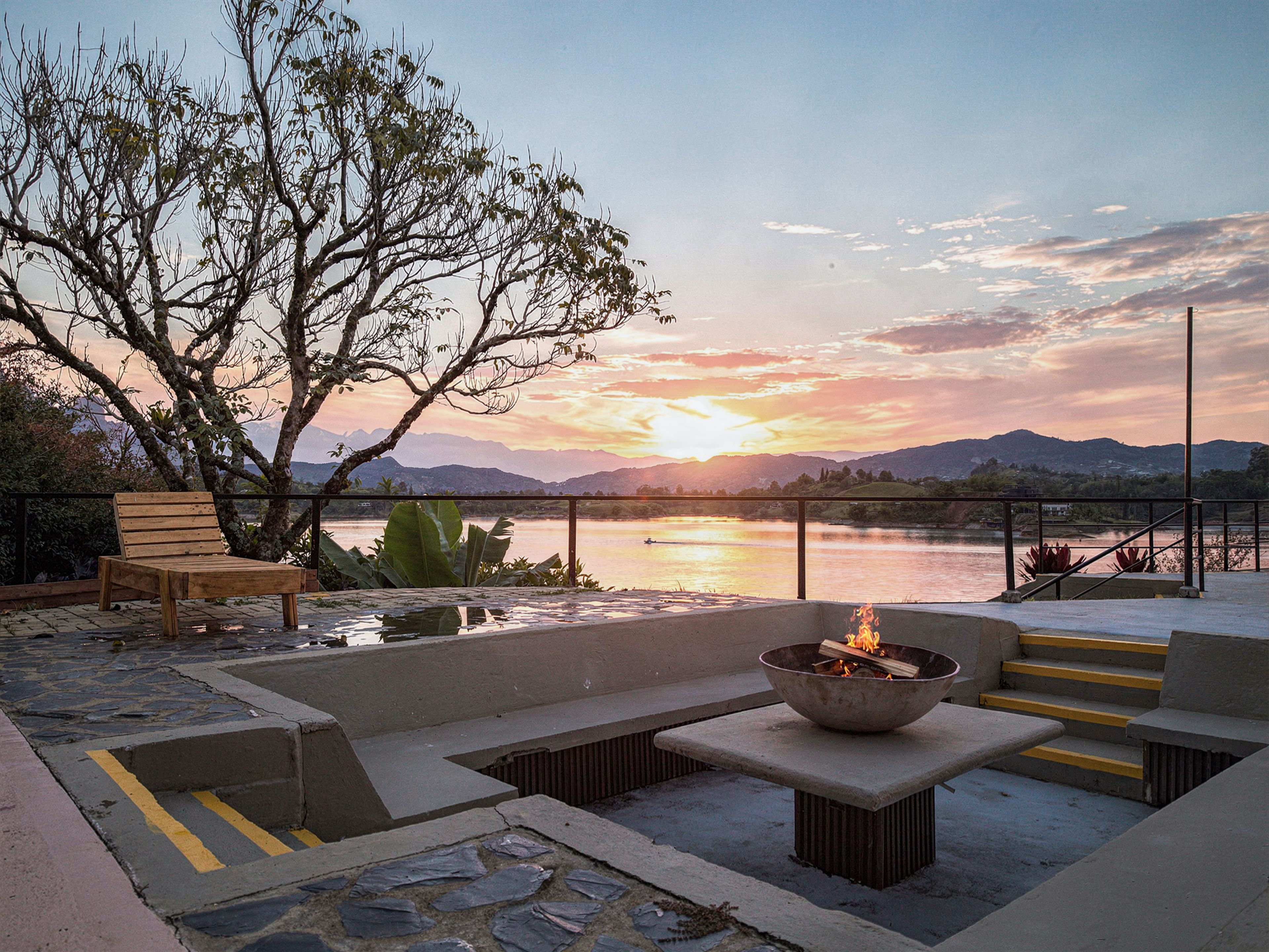 An outdoor seating area with a fire pit, a bench, and a view of a lake at sunset.