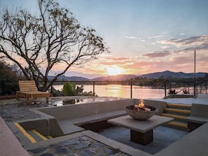 An outdoor seating area with a fire pit, a bench, and a view of a lake at sunset. - Bliss Club (El Peñol)