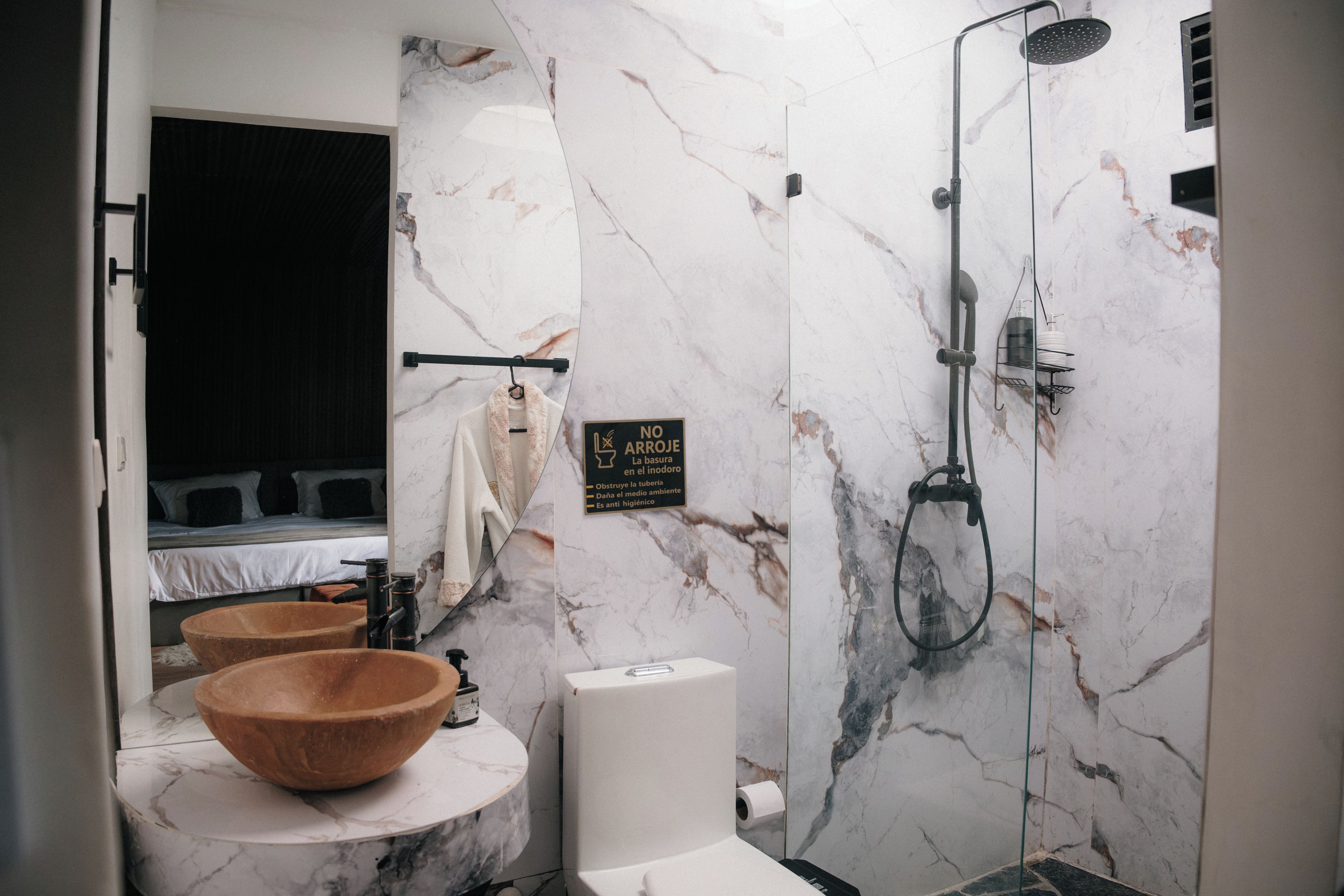 Un baño moderno con pared de mármol, lavamanos de madera, inodoro y ducha.