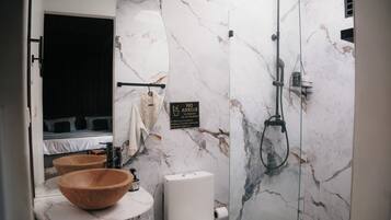Un baño moderno con pared de mármol, lavamanos de madera, inodoro y ducha.