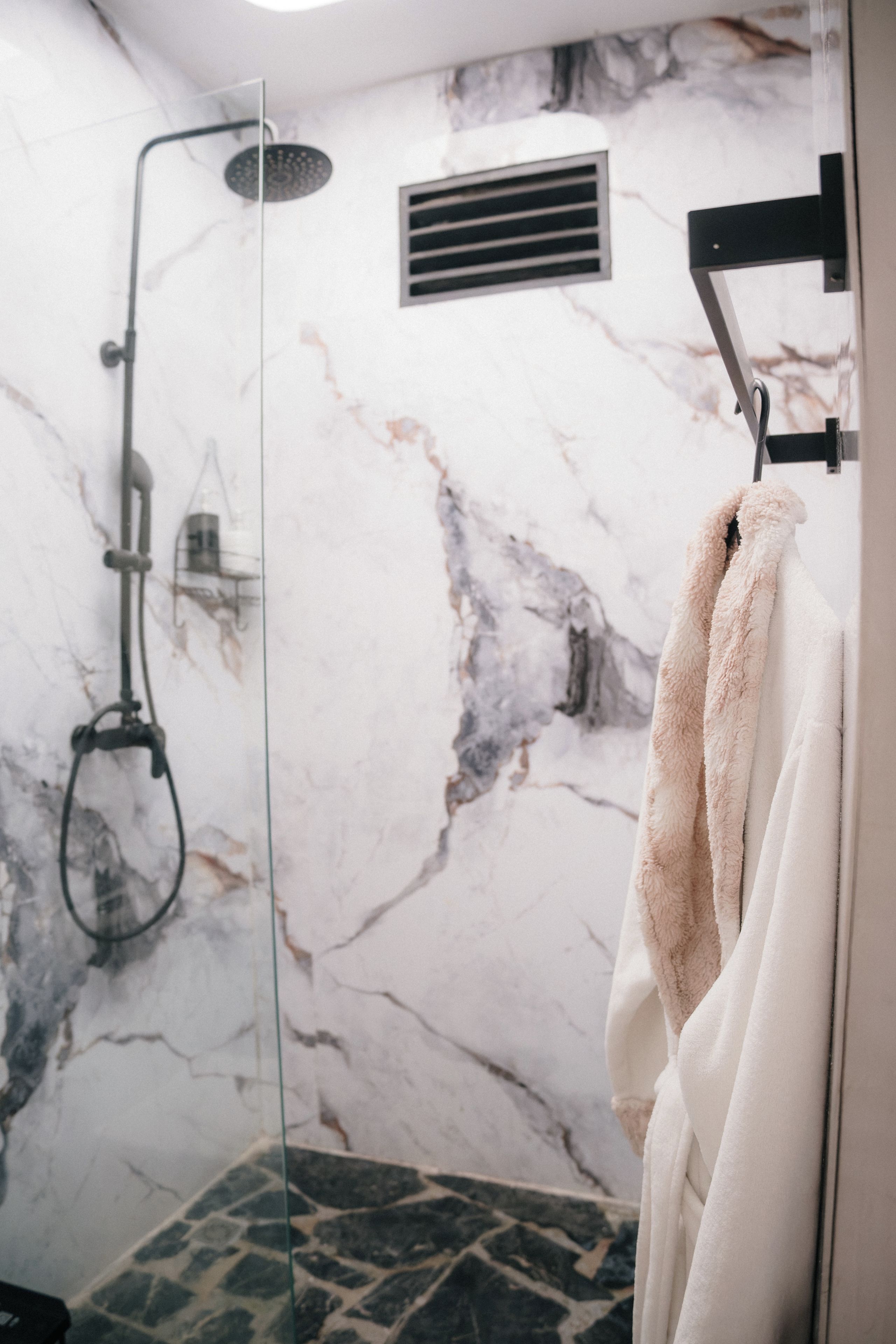 Un baño con cabina de ducha de vidrio, paredes de mármol y un perchero para toallas.