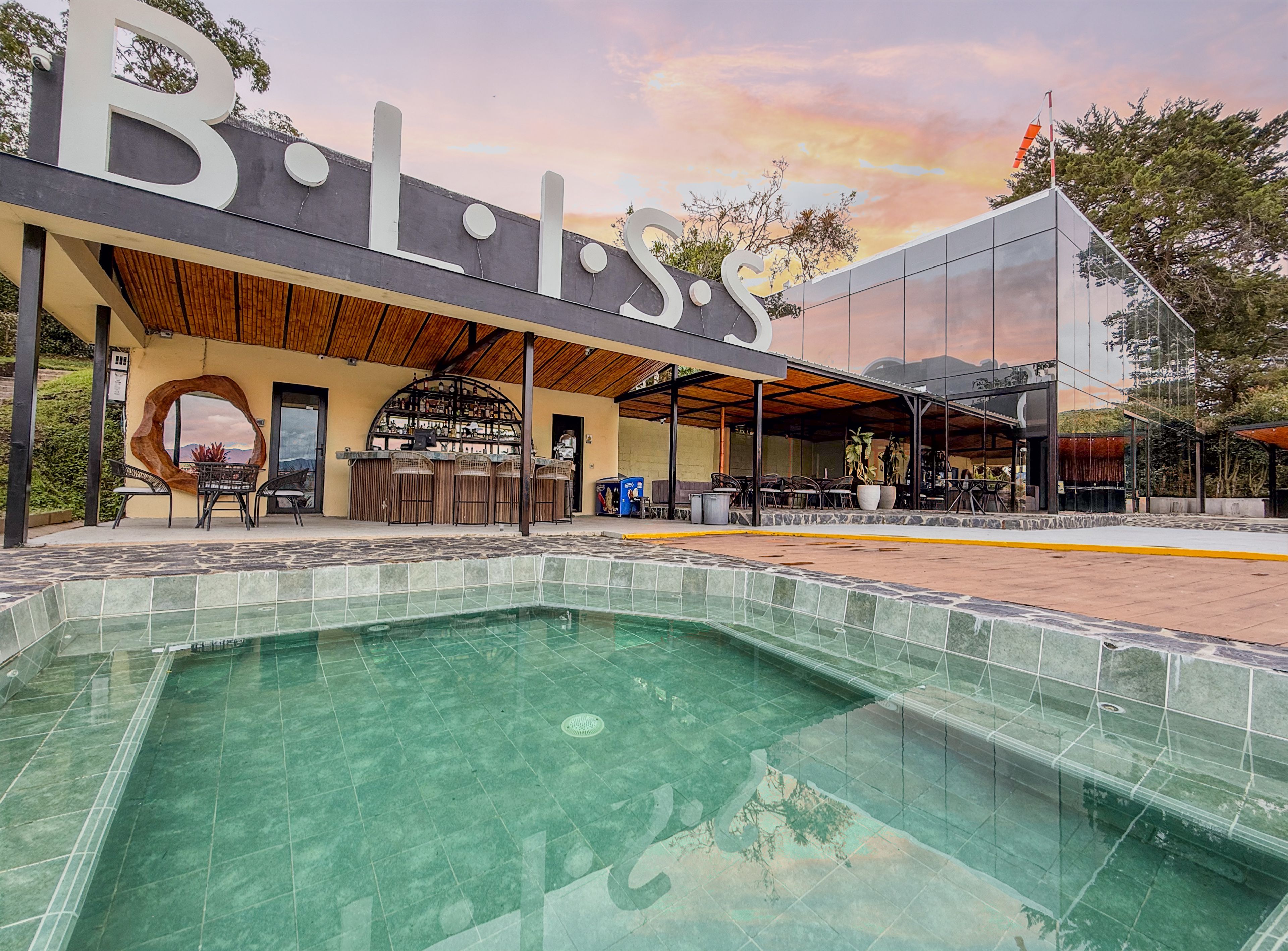 Un espace piscine doté d’un bar et de sièges, entouré d’un bâtiment sur lequel figure un grand panneau avec la lettre « B ».