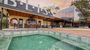 Zona de piscina con bar y asientos, rodeada por un edificio con un gran letrero 'B'.