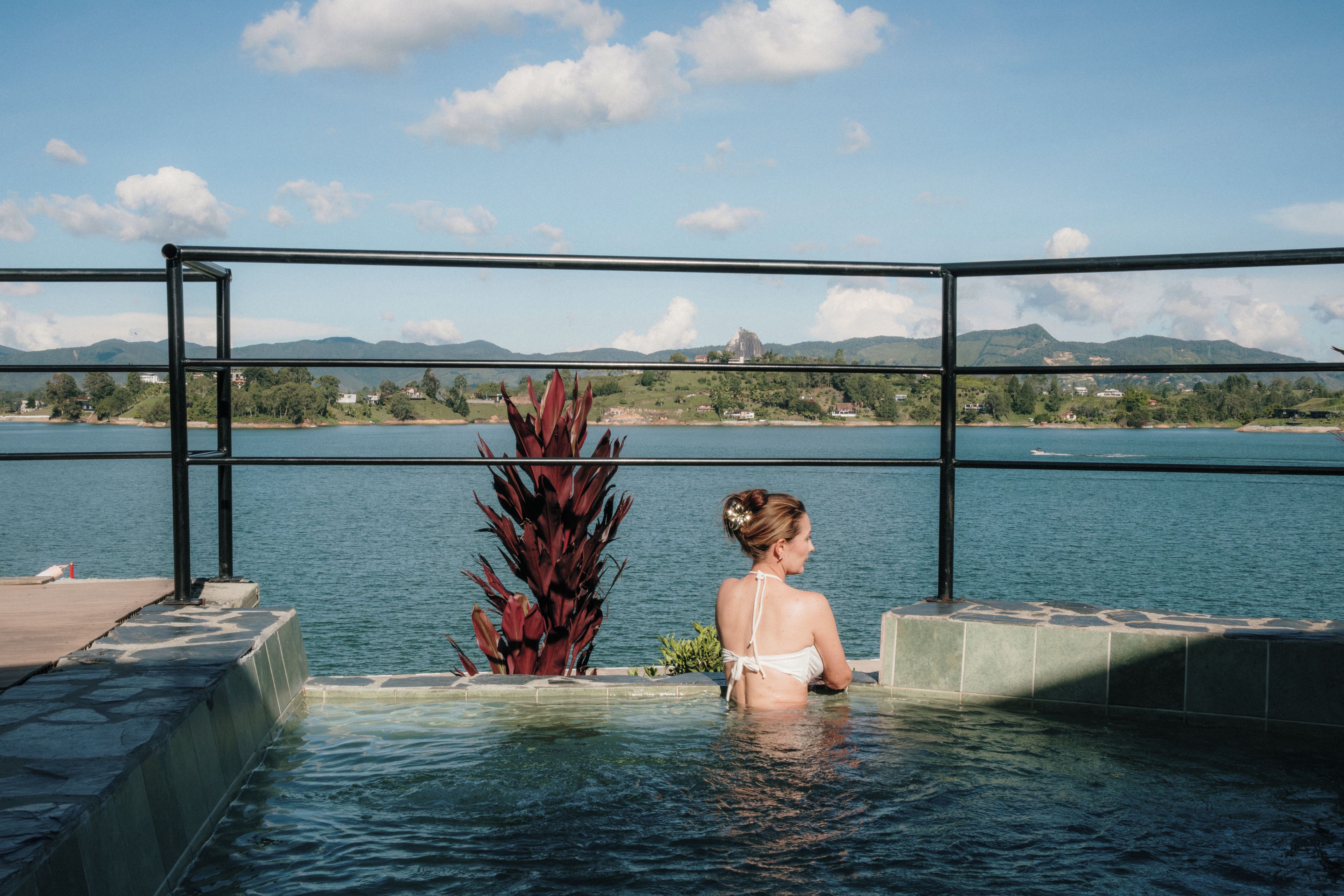 Una persona en una piscina con vistas a un cuerpo de agua y montañas al fondo.