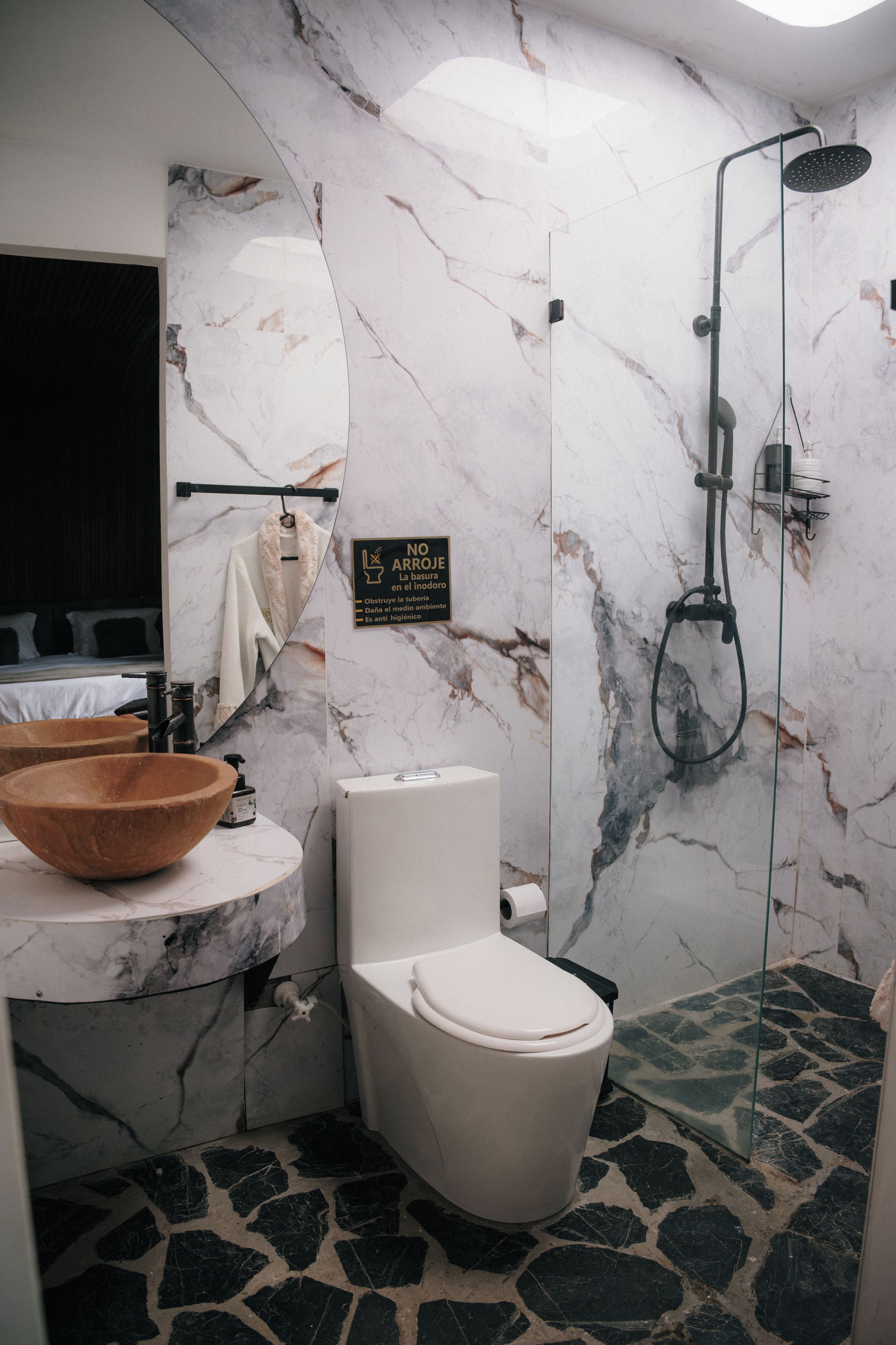 Une salle de bain avec un mur en marbre, un lavabo en forme de bol en bois, des toilettes et une douche.