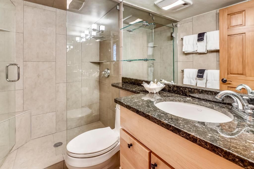 Un baño moderno con cabina de ducha de vidrio, inodoro blanco, lavabo con encimera de mármol y tocador de madera.