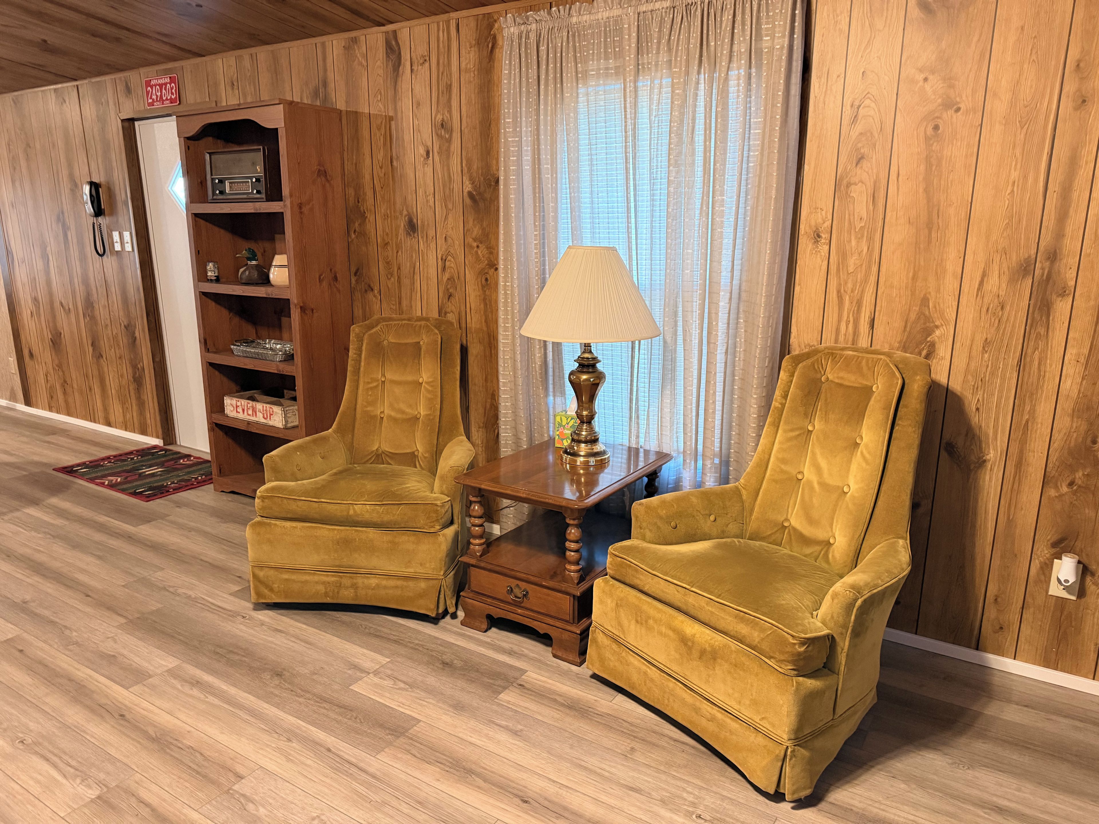 Ein Zimmer mit Holzvertäfelung, zwei Sesseln, einem kleinen Tisch mit Lampe, einem Bücherregal und einem Telefon.