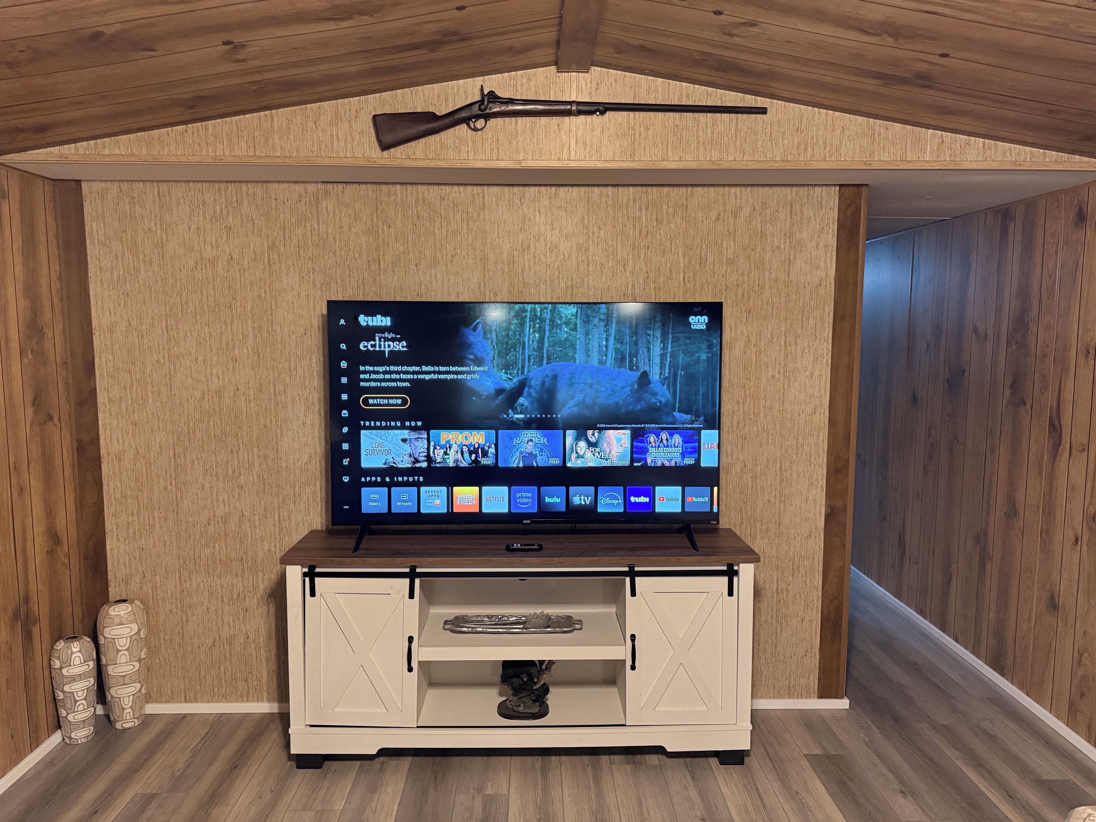 Un televisor montado en una pared de madera con un rifle colgado encima.