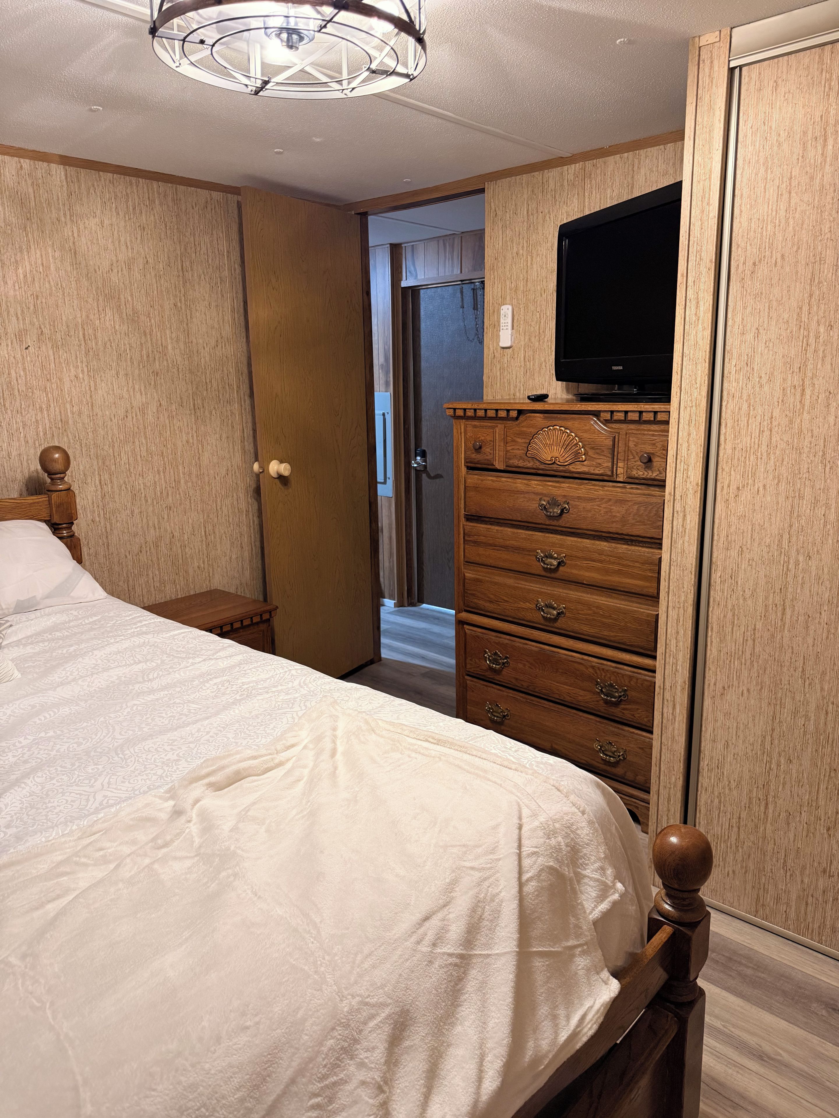 A bedroom with a bed, wooden dresser, and a television on a stand.