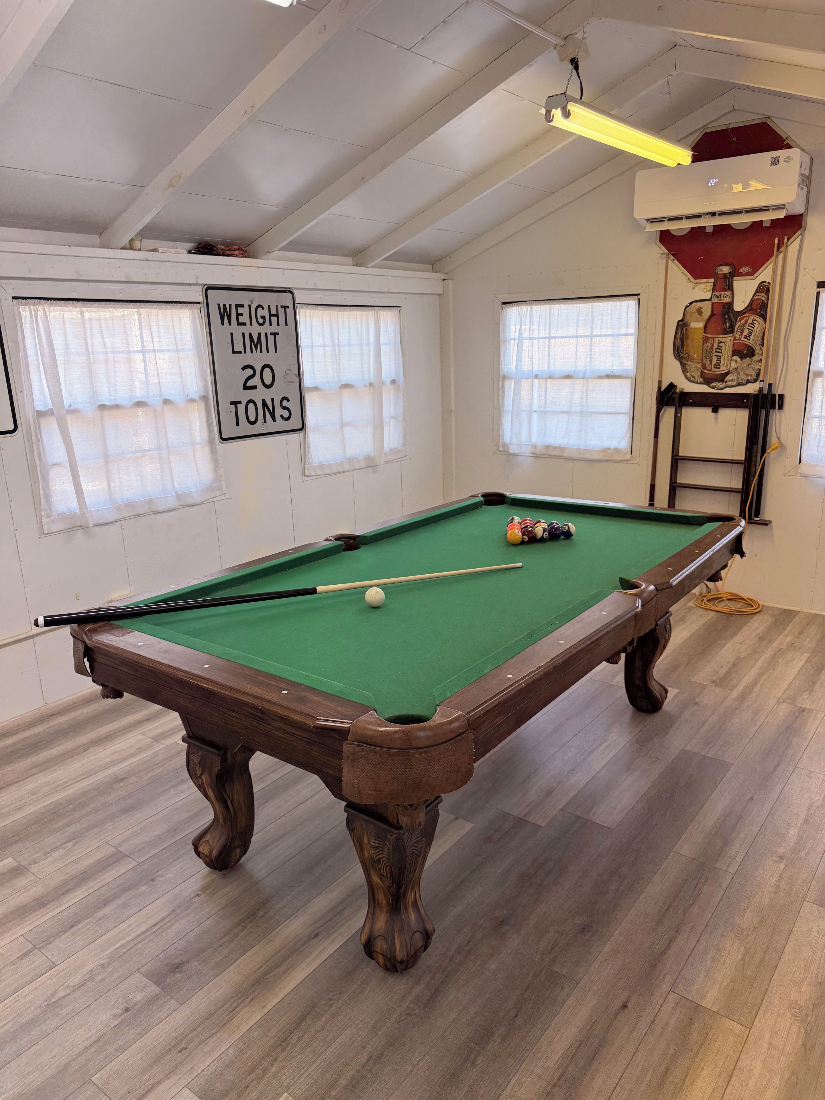 A pool table with a weight limit sign, wooden flooring, and a ceiling fan.