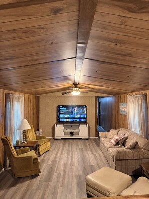 Una sala de estar con techo de madera, televisor, sofá, silla y mesa.