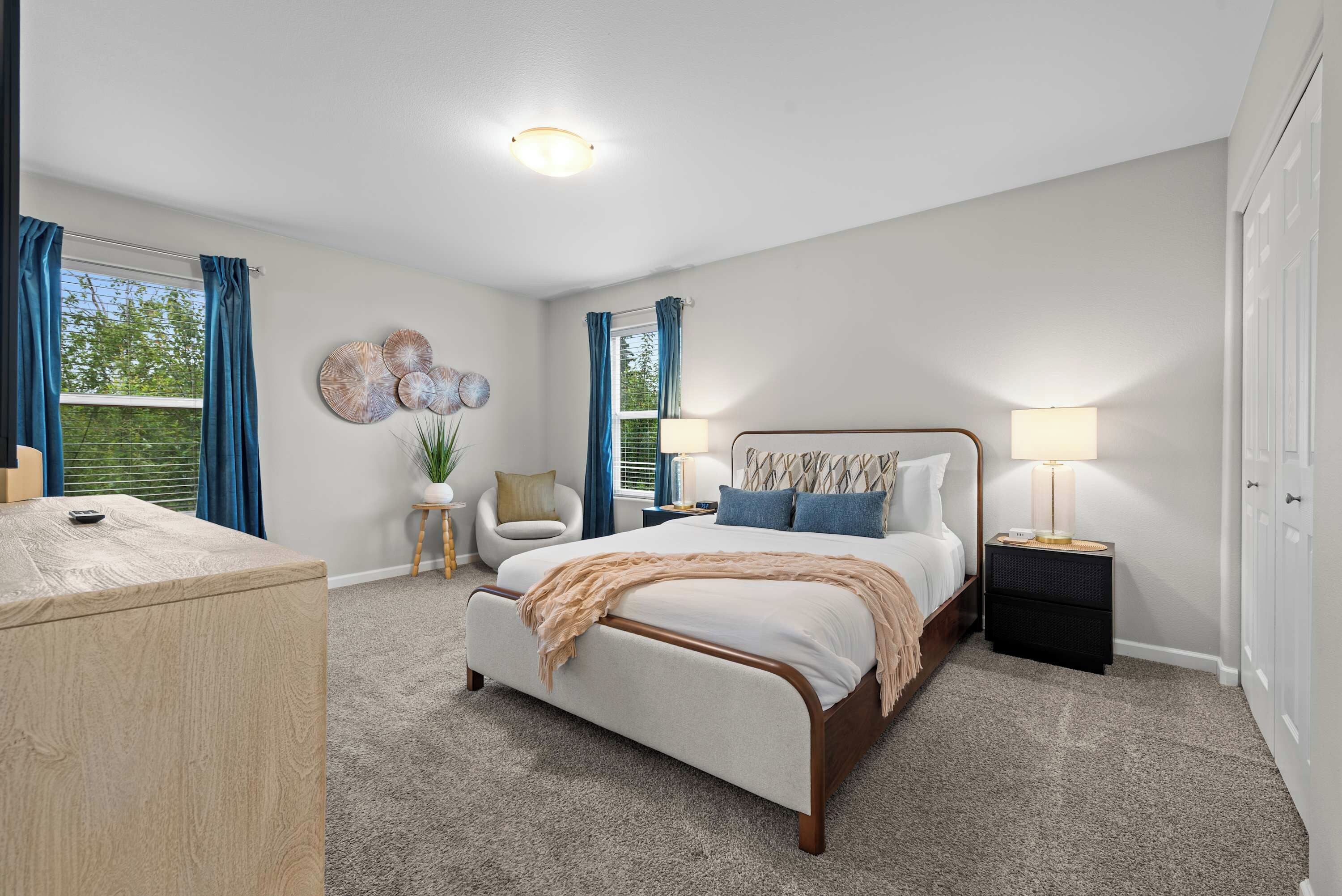 A bedroom with a bed, bedside tables, a dresser, and a wall-mounted light fixture.