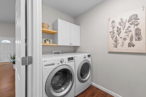 A laundry room with two front-loading LG washers, a white cabinet above, and a botanical illustration on the wall. - Quiet 3BR Getaway w/ Full Kitchen & Laundry! (Wasilla)