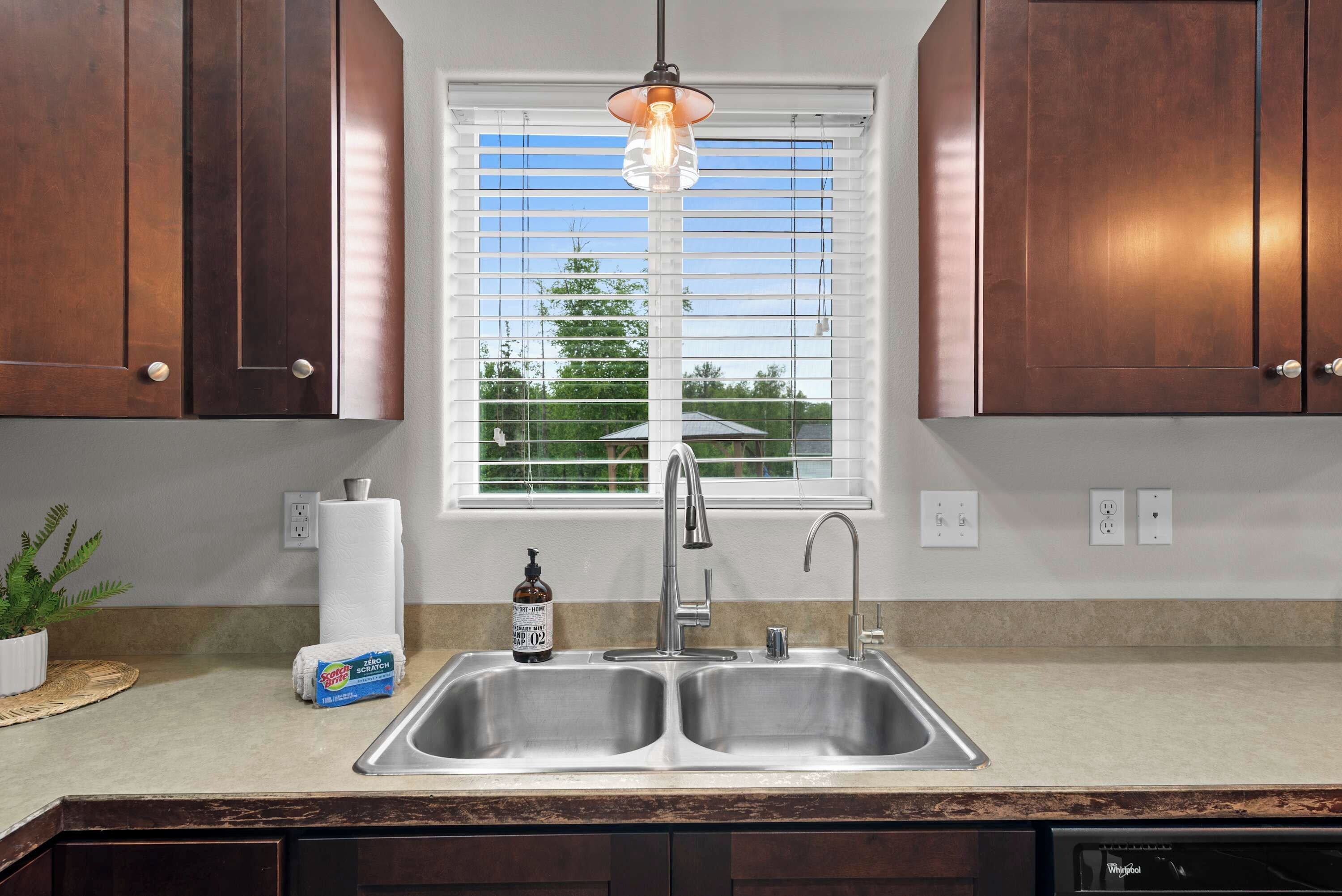 A kitchen with a double sink, a window with blinds, and a hanging pendant light.