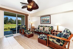 Una sala de estar con un gran ventanal corredizo que da a un patio, un ventilador de techo, un cuadro enmarcado y una lámpara.