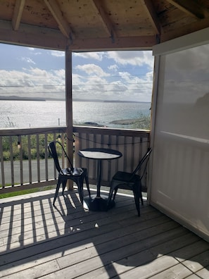 Un espace extérieur abrité, doté d’une table et de chaises, d’où l’on peut admirer un plan d’eau et un paysage lointain.