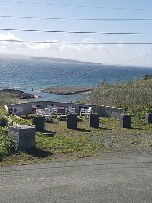 A coastal area with a seating area featuring chairs and tables, a flag, and a view of the sea and distant land. - Rose Castle Inn & Café. Beautiful, breathtaking views of the ocean. (Bell Island)