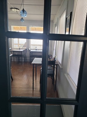 A room with a dining area, a table, chairs, a ceiling light fixture, and windows with blinds. - Rose Castle Inn & Café. Beautiful, breathtaking views of the ocean. (Bell Island)
