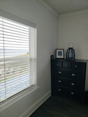 A room with a window with blinds, a dark dresser with drawers, and a framed picture on top. - Rose Castle Inn & Café. Beautiful, breathtaking views of the ocean. (Bell Island)