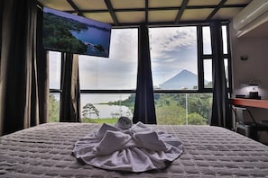 Habitació d'hotel amb llit, televisió penjada a la paret i vista d'una muntanya i un llac.
