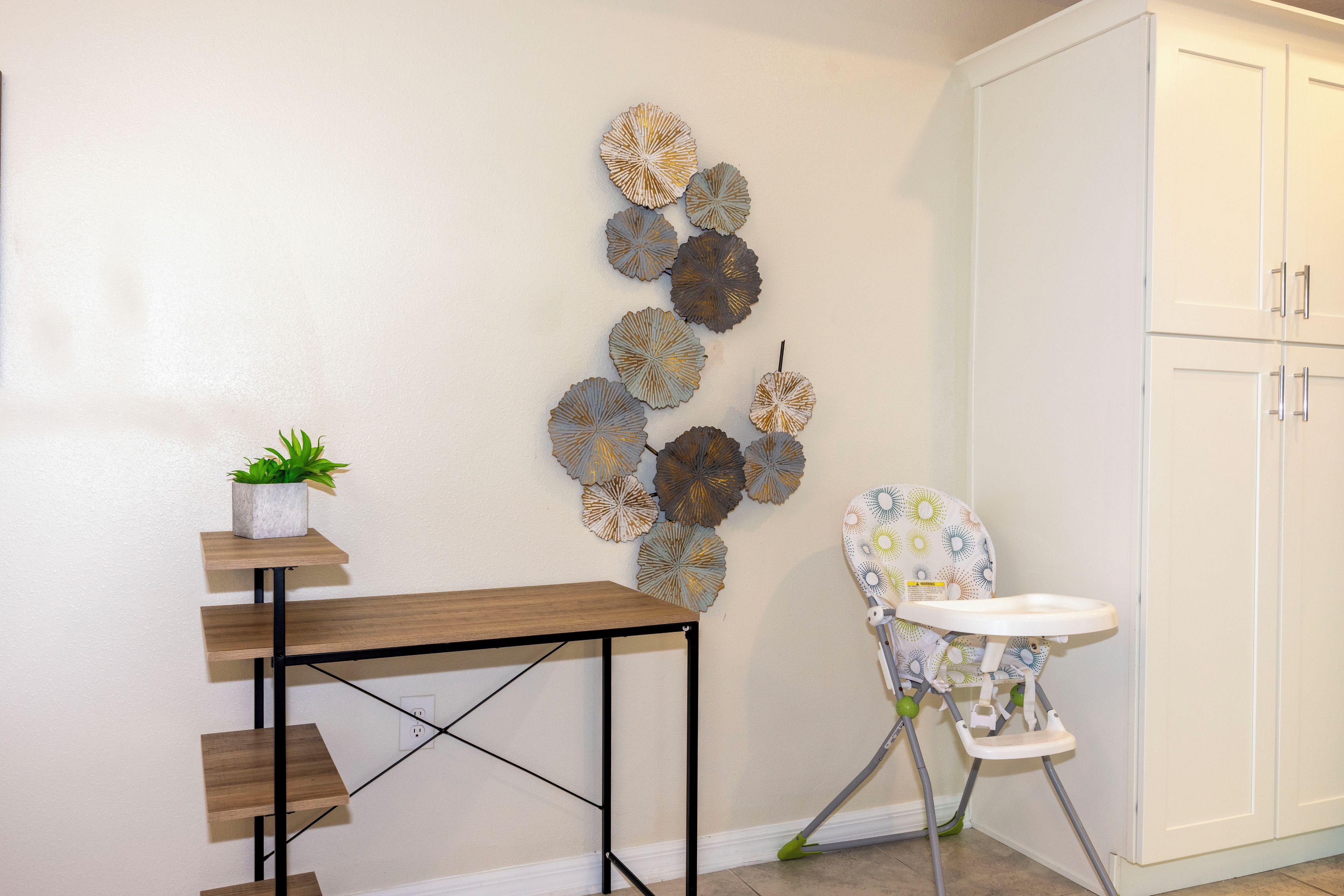 A kitchen with a white cabinet, a wooden table with a potted plant, and a decorative wall piece.