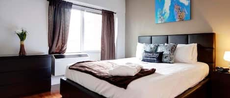 A modern bedroom with a large bed, dark headboard, and a window with curtains.