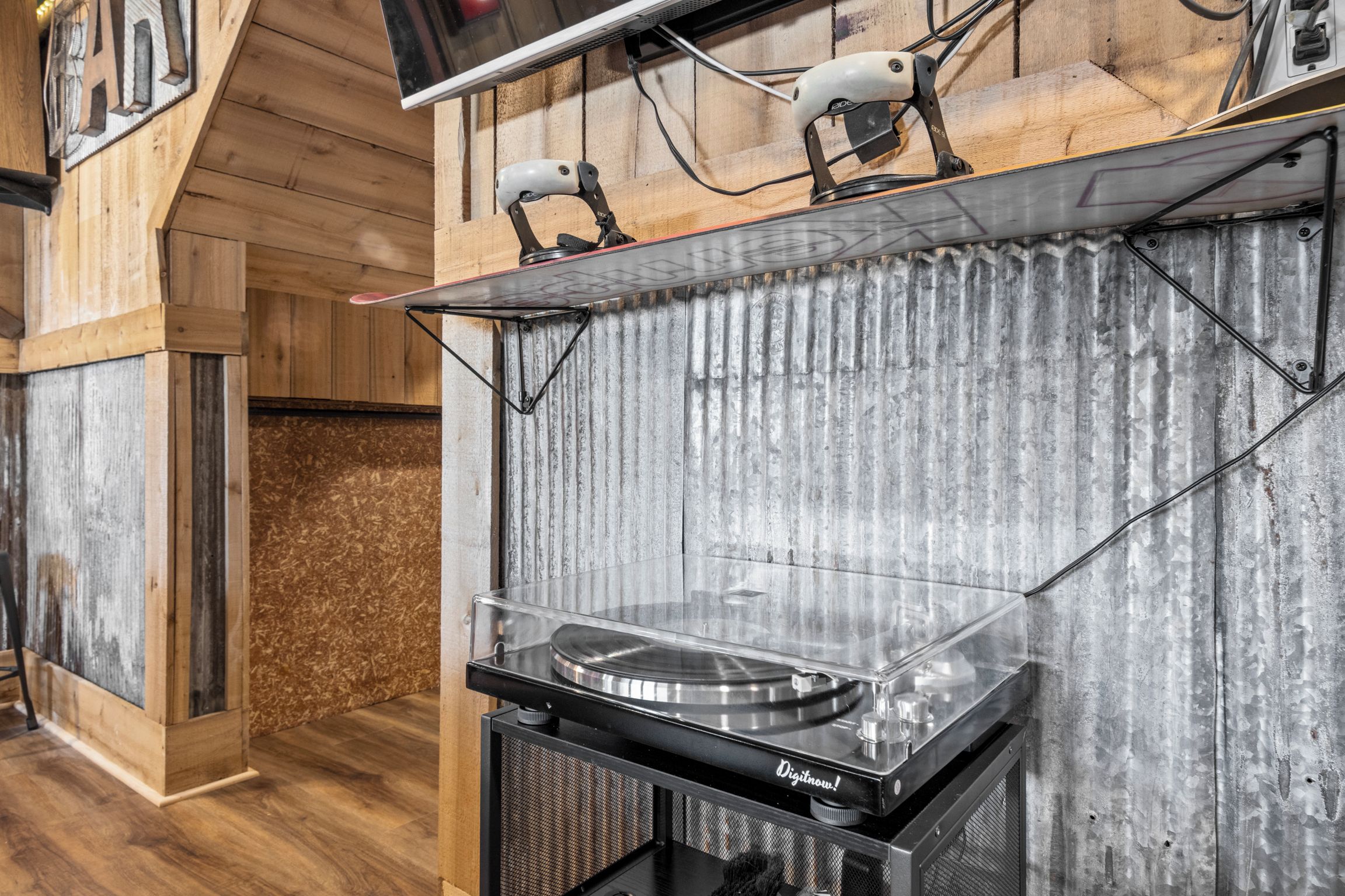 A DJ setup with a turntable, mixer, and speakers in a room with wooden walls and a corrugated metal accent wall.