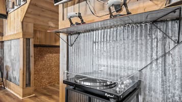 A DJ setup with a turntable, mixer, and speakers in a room with wooden walls and a corrugated metal accent wall.