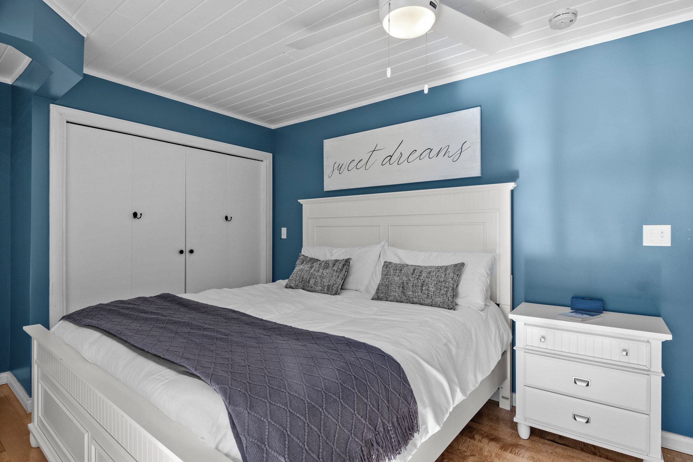 Ein Schlafzimmer mit Bett, Nachttisch, Kommode und einer Wand mit einem Schild.