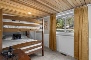 Quarto com beliche, janela e vista para árvores.