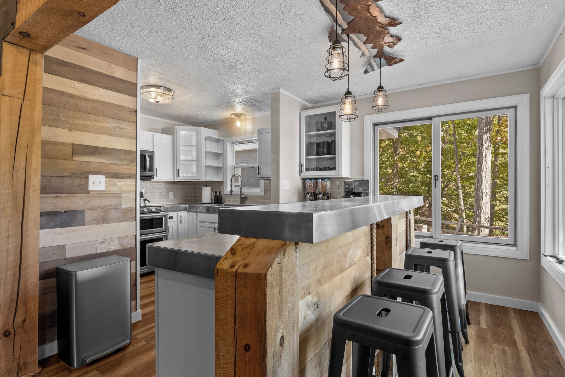 Une cuisine moderne dotée d’un îlot central, de tabourets de bar et d’une grande fenêtre offrant une vue sur les arbres.
