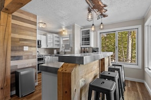 A modern kitchen with a central island, bar stools, and a large window with a view of trees.