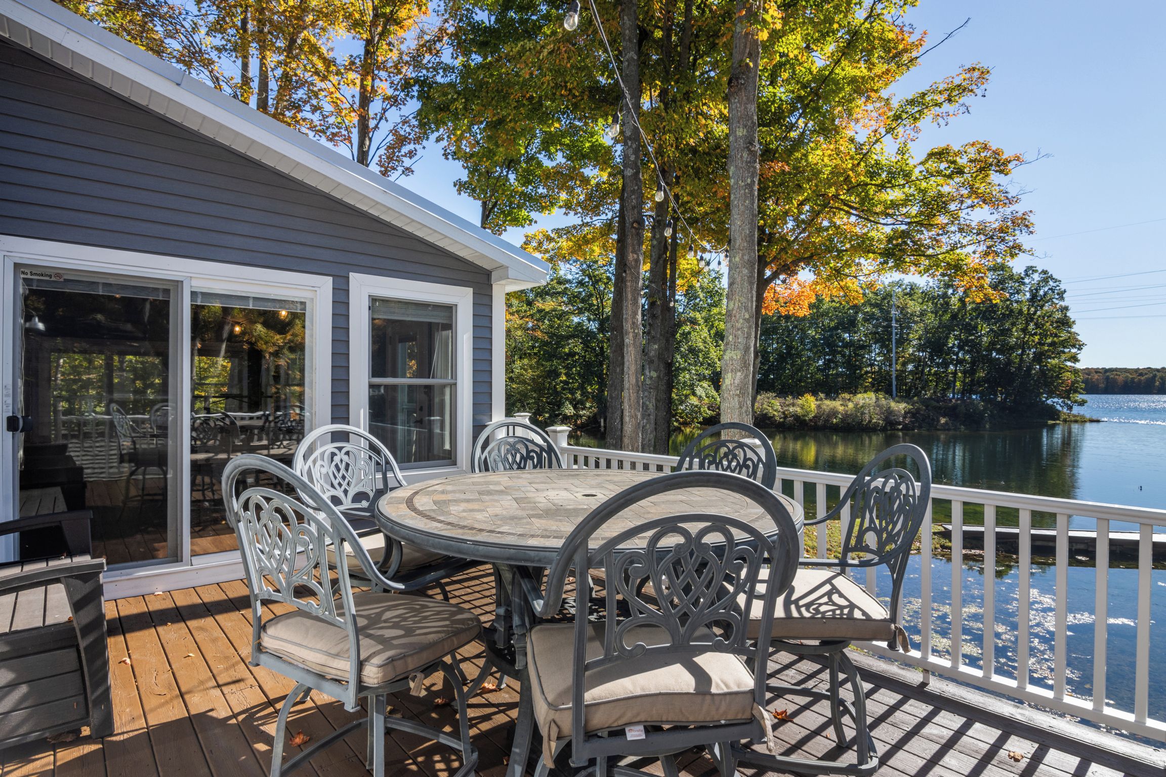 Une terrasse dotée d’une table ronde et de chaises, offrant une vue sur un plan d’eau et entourée d’arbres aux feuilles d’automne.