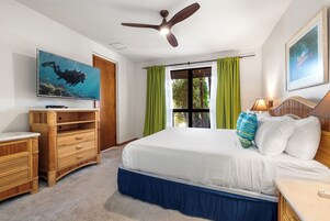 Un dormitorio con cama, televisor, ventilador de techo y ventana con cortinas.