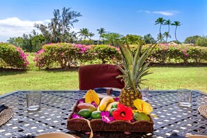 Mesa servida con frutero, piña y vasos, con vista a un jardín y palmeras.