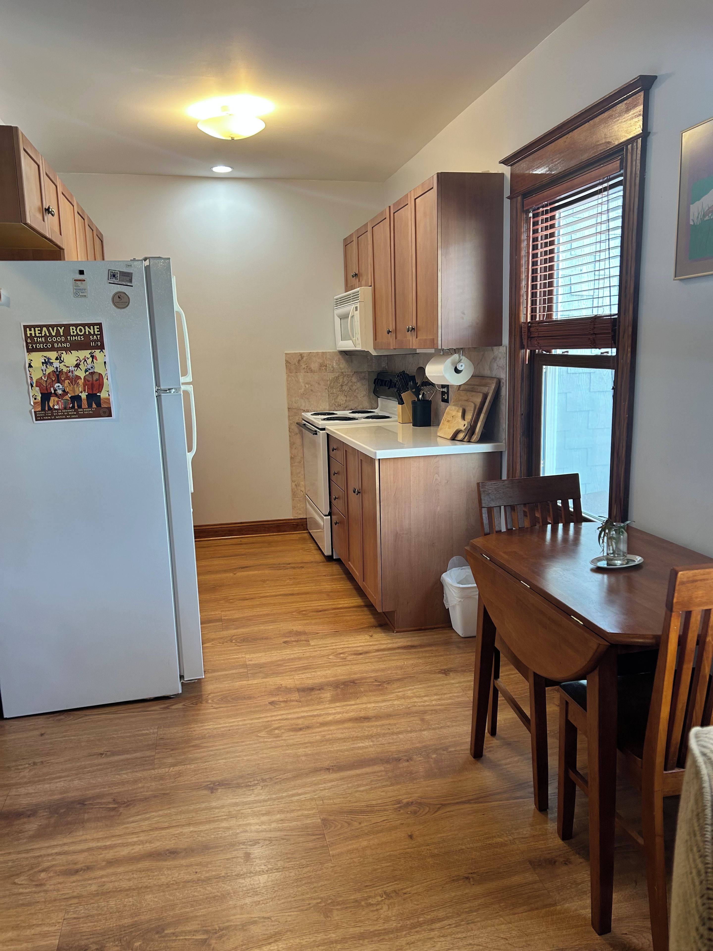 A compact kitchen with wooden cabinets, a white refrigerator, a stove, and a dining table with chairs.