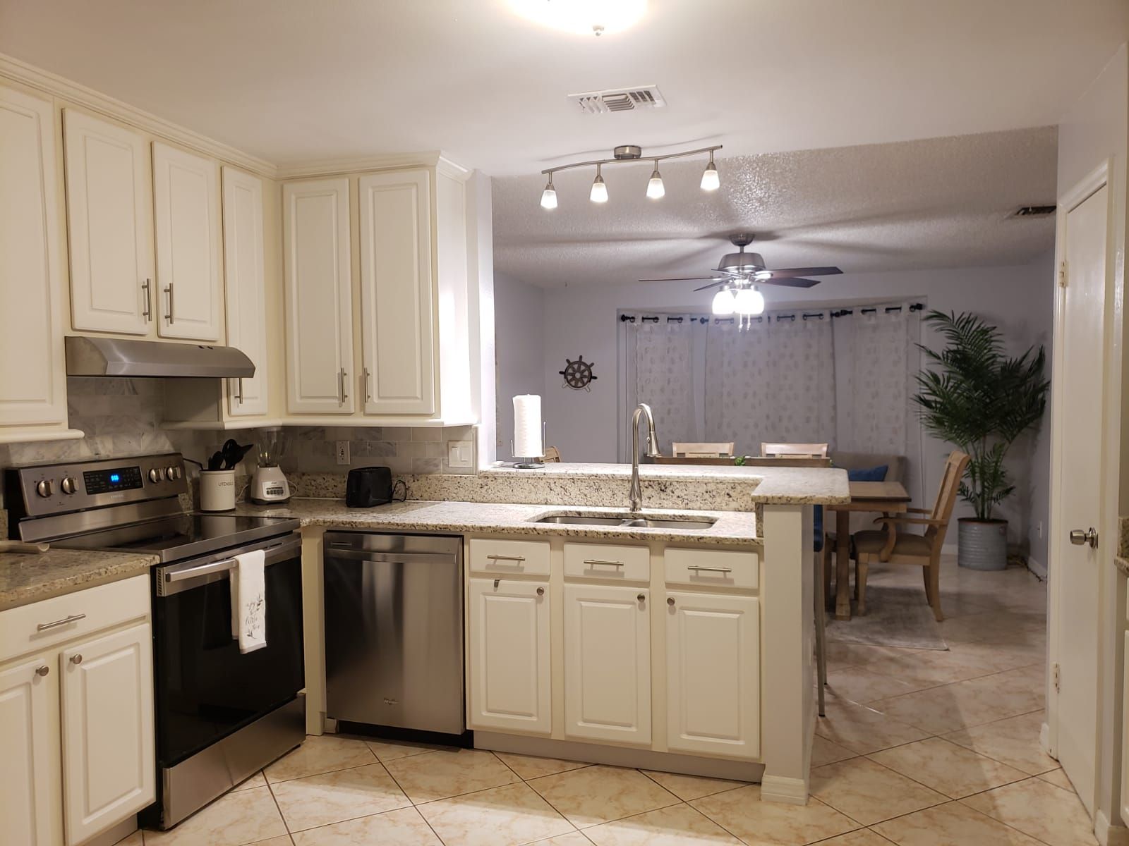 A kitchen with white cabinets, a stove, a dishwasher, and a ceiling fan.