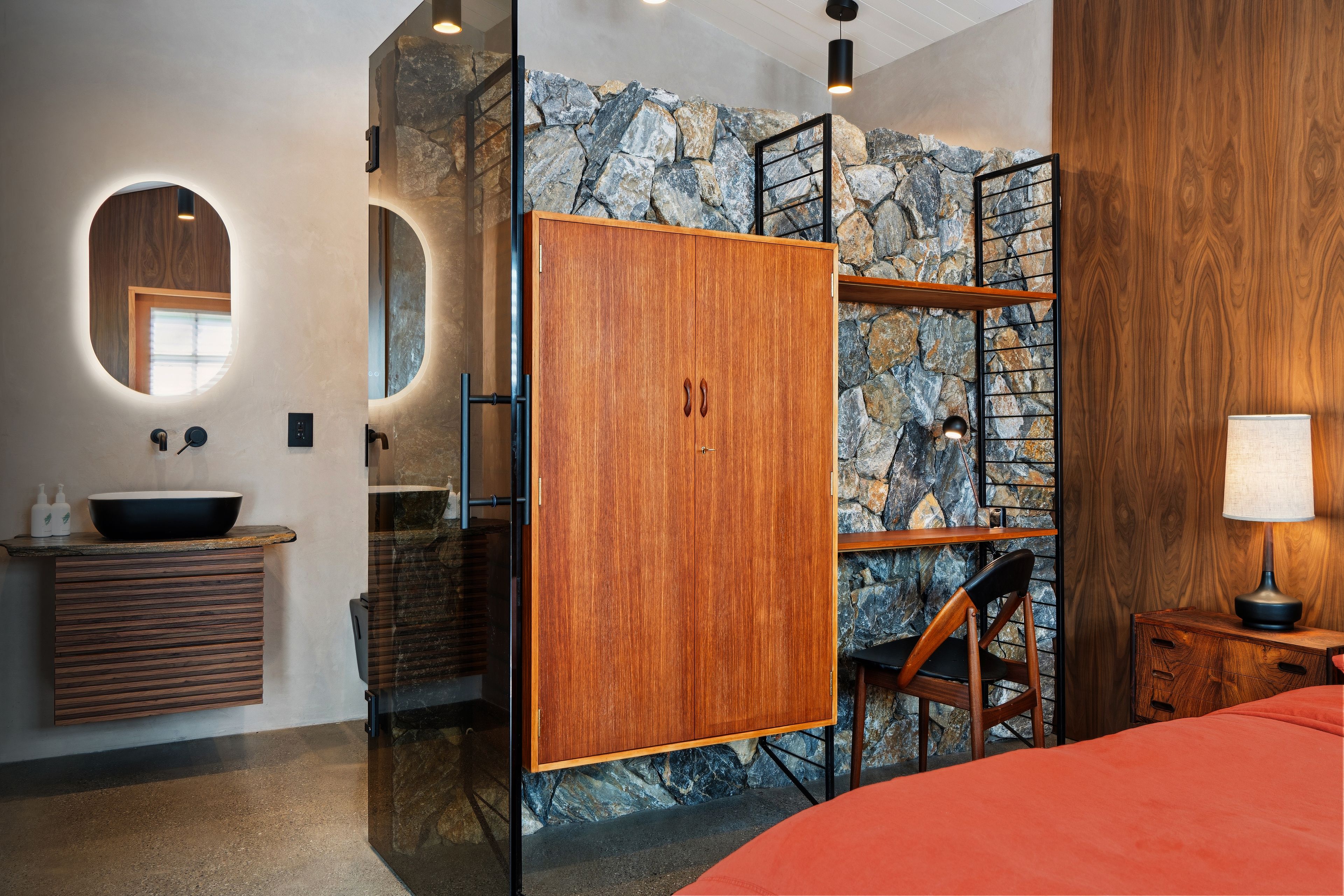 Un baño moderno con pared de piedra, armarios de madera, un lavamanos y un espejo.