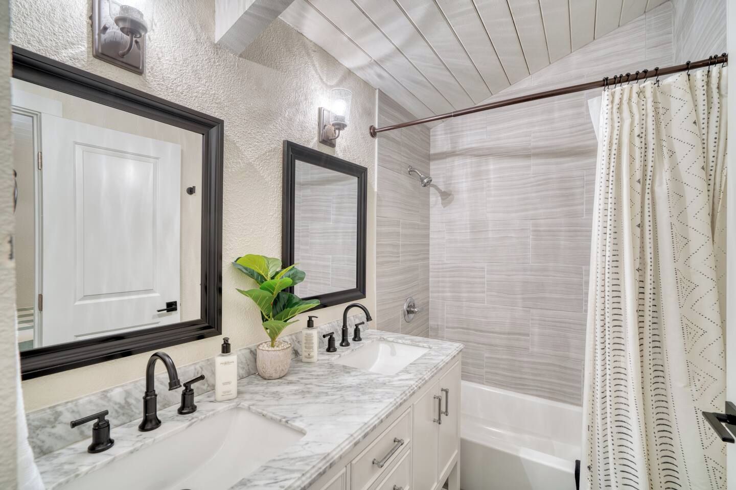 A bathroom with two sinks, a mirror, a shower, and a curtain.