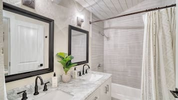 A bathroom with two sinks, a mirror, a shower, and a curtain.