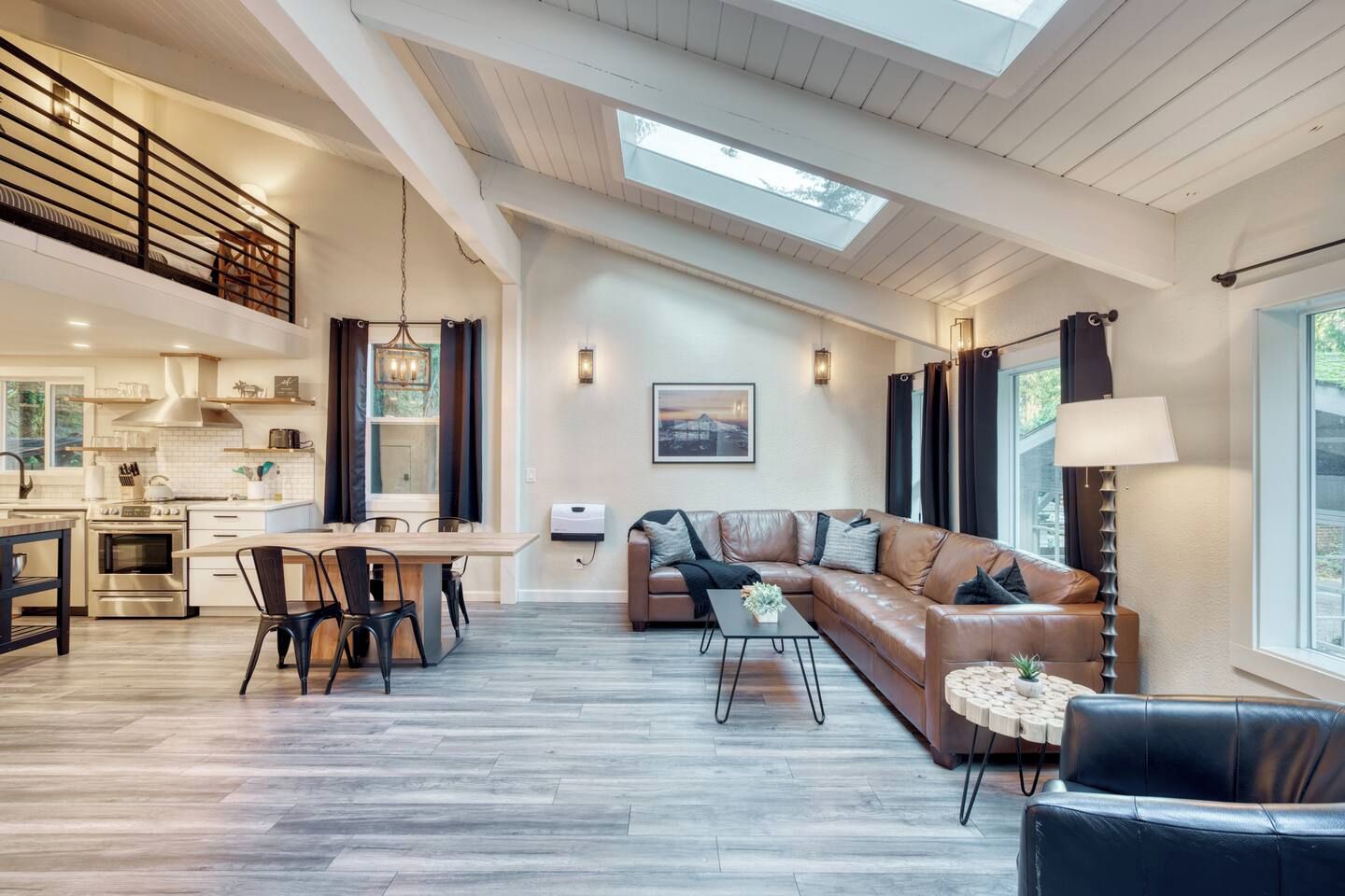 A spacious living area with a high ceiling, a dining table, a sofa, and a view of the outdoors.